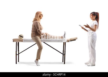 Fisioterapista in uniforme bianca che tiene un appunti e parla con una paziente isolata su sfondo bianco Foto Stock