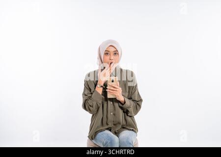 Una giovane donna in uno studio possiede uno smartphone, esprimendo gioia ed eccitazione Foto Stock