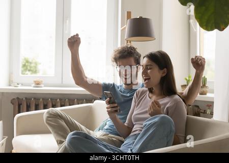 Una coppia innamorata festeggia la vittoria guardando lo schermo dello smartphone Foto Stock