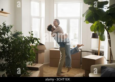 Felice giovane coppia che ride abbracciando festeggia il trasloco in un nuovo appartamento Foto Stock