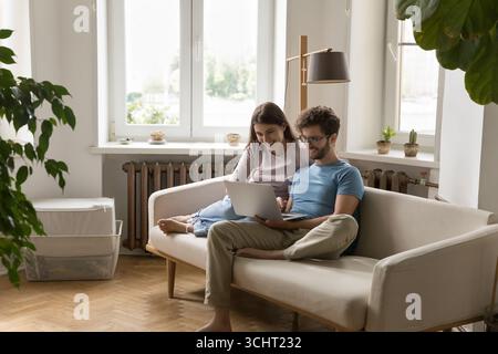 Una giovane coppia di famiglie rilassata che utilizza un notebook in un soggiorno accogliente Foto Stock