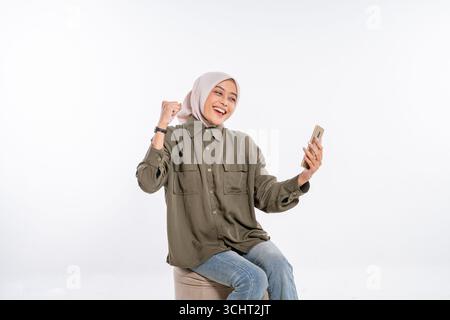 Una giovane donna allegra che indossa un hijab sta prendendo un Selfie con il suo smartphone Foto Stock
