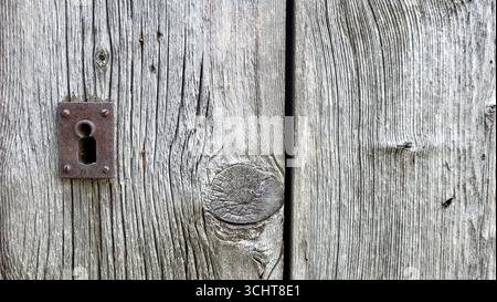 Primo piano di una vecchia serratura arrugginita in una porta in legno grigio-nero invecchiato. Una fotografia rustica dettagliata che cattura texture e fascino vintage Foto Stock