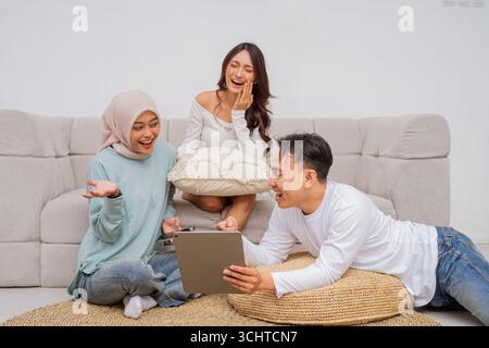 Gli amici si divertono insieme in un salotto accogliente con un tablet Foto Stock