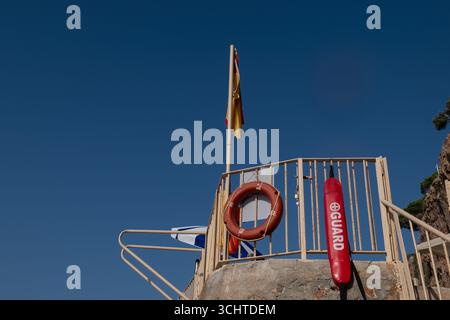 Stazione di salvataggio con equipaggiamento di salvataggio e bandiere in una giornata di sole, simboleggiando la sicurezza costiera e la vigilanza per i naviganti. Foto Stock