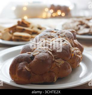 Tradizionale vanocka ceca pane natalizio intrecciato con mandorle e zucchero a velo servito su un piatto bianco con sfondo di biscotti linzer Foto Stock