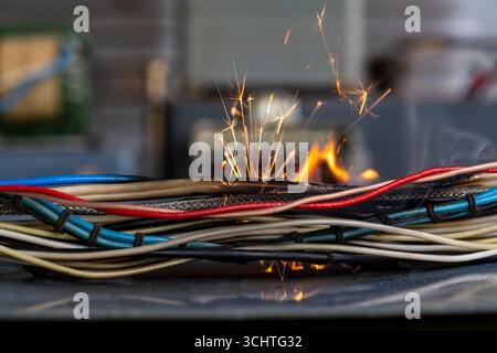 Fiamme, scintille, fumo tra i cavi elettrici, primo piano. Cortocircuito nei fili intrecciati dei dispositivi elettrici, concetto di rischio di incendio Foto Stock