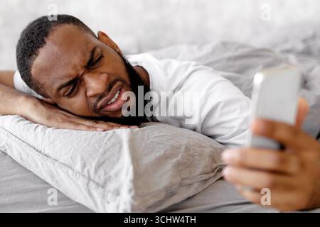 Uomo nero che soffre di insonnia guardando il telefono a letto Foto Stock