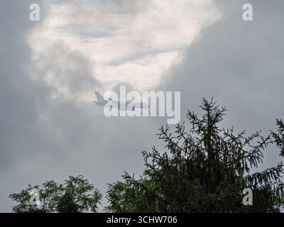 Un aereo passeggeri Emirates Airbus A380 vola attraverso un cielo spettacolare e nuvoloso con alberi in primo piano. Foto Stock