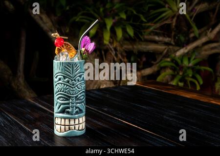 Un rinfrescante cocktail tiki in un bicchiere di ceramica blu-grigio, decorato con una ciliegia rossa, agrumi secchi e un'orchidea. Foto Stock