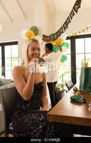 Donna bionda sorridente alla festa di compleanno mentre l'uomo decora con palloncini, a casa Foto Stock