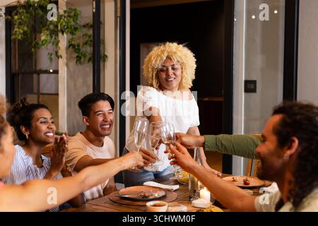 Brindisi con champagne, amici diversi che festeggiano con gioia a cena insieme, sul patio Foto Stock