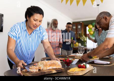 Gruppi diversi di amici anziani che si divertono a preparare i pasti insieme a casa, condividendo i sorrisi Foto Stock