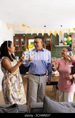 Festeggia a casa, un gruppo di amici anziani che brinda con bicchieri da vino, sorridendo Foto Stock