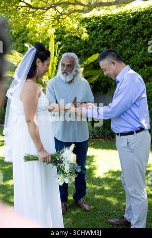 Si scambiano anelli, diverse coppie con l'officiante durante la cerimonia di nozze in giardino Foto Stock