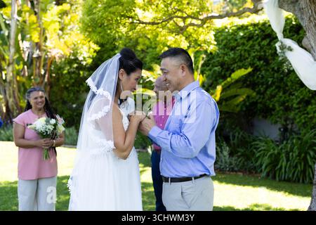 Scambio di voti, sposi e sposi diversi sorridono e tengono per mano in giardino Foto Stock