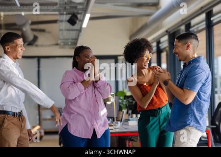 In ufficio, colleghi diversi che celebrano il successo, condividendo momenti di gioia insieme Foto Stock