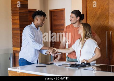 Agente immobiliare che stringe la mano alla coppia in una cucina moderna, finalizzando l'accordo Foto Stock