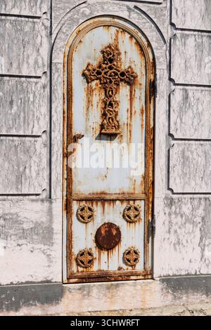 Una porta di metallo arrugginita e intemprata con un intricato disegno a croce su una tomba del cimitero di Prazeres a Lisbona, in Portogallo, che mostra la bellezza dell'età e dei dettagli. Foto Stock