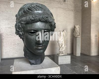Antica testa in bronzo di un giovane greco in mostra nel Glyptothek di Monaco, con sculture in marmo classiche sullo sfondo. Foto Stock