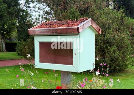 Una piccola biblioteca libera in legno con un tetto verde piantato con succulente sorge in un giardino pubblico. Sostenibilità comunitaria, tetti verdi micro, eco Foto Stock