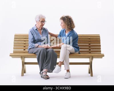 Infermiere professionale che conforta una donna anziana triste e confusa, sono seduti su una panchina, isolati su sfondo bianco Foto Stock
