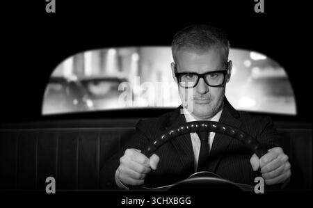Uomo d'affari in stile vintage che tiene il volante e guida la sua auto, film noir Foto Stock