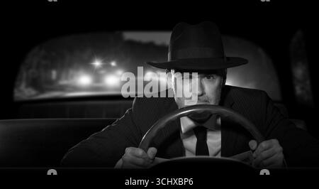 Un criminale con un cappello che fugge dalla polizia di notte mentre guida la sua auto. stile film noir anni '1950. Foto Stock