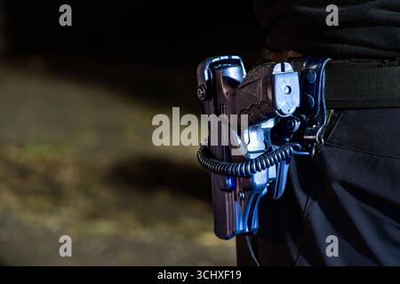 Landkreis Osnabrück, Deutschland 04. Giu 2025: IM Bild: Detailaufnahme einer Polizeiwaffe im Holster bei nächtlichem Einsatz. Die Dienstpistole ist zusätzlich mit einer Sicherheitsvorrichtung versehen: eine Sicherungsspirale verbindet die Waffe mit dem Gürtel und schützt vor unbefugtem Zugriff oder Entwendung. Symbolbild für Sicherheit, Polizeiausrüstung und den geschützten Umgang mit Schusswaffen im Polizeidienst. Niedersachsen *** Distretto di Osnabrück, Germania 04 giugno 2025 Vista dettagliata di un'arma della polizia in una fondina durante le operazioni notturne la pistola di servizio è inoltre equipaggiata Foto Stock