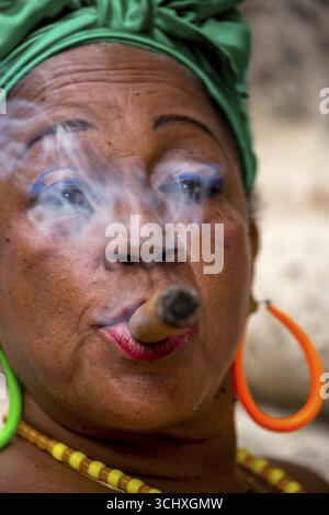 La vecchia donna cubana con arco di capelli verdi fuma un sigaro dell'Avana, la donna cubana con sigaro e unghie laccate con bandiera cubana, bandiera cubana, bastoncini di unghie Foto Stock