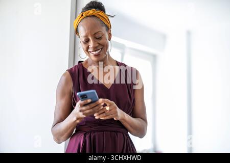 Ritratto di una donna d'affari sorridente che usa il telefono cellulare in ufficio Foto Stock