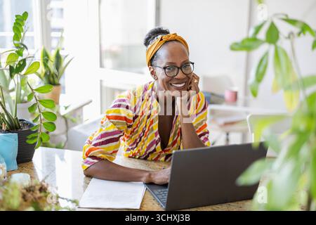 Donna sorridente che utilizza un notebook mentre è seduta alla scrivania in ufficio Foto Stock