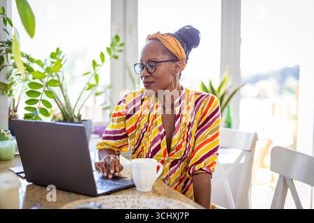 Donna felice che beve caffè e usa un computer portatile a casa Foto Stock