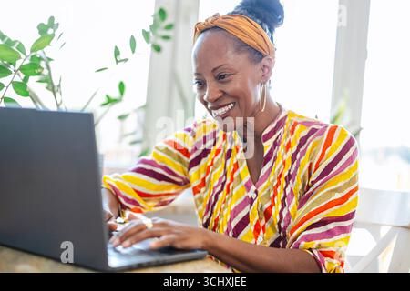 Donna sorridente che utilizza un notebook mentre è seduta alla scrivania in ufficio Foto Stock