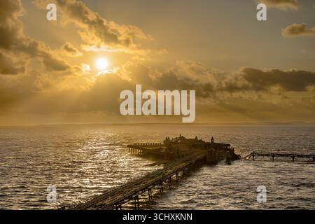 Il sole tramonta al vecchio molo di Birnbeck a Weston Super Mare, Somerset, Regno Unito, con i raggi del sole che scendono. Il molo è impostato per essere ripristinato. Foto Stock