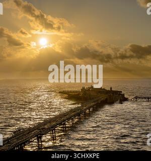 Il sole tramonta al vecchio molo di Birnbeck a Weston Super Mare, Somerset, Regno Unito, con i raggi del sole che scendono. Il molo è impostato per essere ripristinato. Foto Stock
