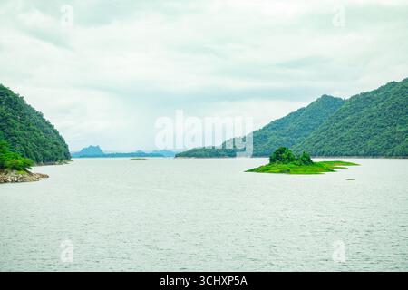 Un'ampia vista panoramica di una diga idroelettrica circondata da lussureggianti montagne verdi e fitte foreste, che simboleggiano l'energia pulita e l'energia rinnovabile, Foto Stock