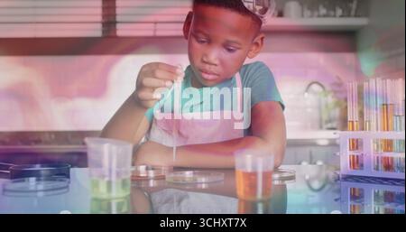 Ragazzo che indossa un grembiule che conduce esperimenti in cucina, con contagocce, piastre di Petri e provette per test Foto Stock