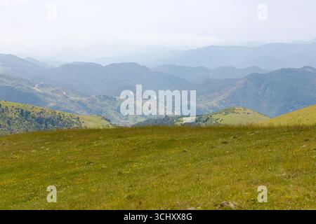 Distanti crinali di montagna e strade tortuose viste dall'altopiano di Creueta, con pendii verdi e un cielo nebbioso sui Pirenei in estate. Foto Stock