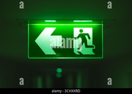 Uscita direzione freccia direzione direzione, segnale guida uscita luce verde segnale uscita di emergenza in una stanza buia installazione sul corridoio dell'edificio a soffitto corri Foto Stock
