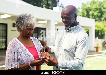 Coppie senior diverse che si scambiano anelli in giardino, celebrando l'amore e l'impegno insieme Foto Stock