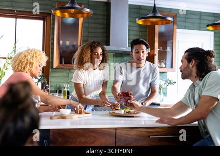Amici giovani e variegati che si godono il brunch, condividono cibo e risate nella cucina moderna, a casa Foto Stock