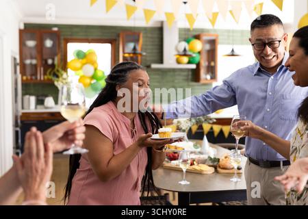Fai esplodere la candela sul cupcake, donna che festeggia il compleanno con diversi amici, a casa Foto Stock