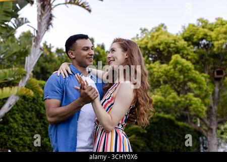 Giovani coppie diverse che ballano gioiosamente in giardino, circondate da lussureggiante vegetazione, spazio copia Foto Stock