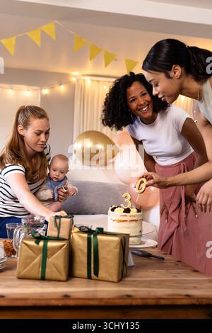 Festeggiamo il compleanno, le diverse amiche con il bambino si godono torte e regali a casa Foto Stock