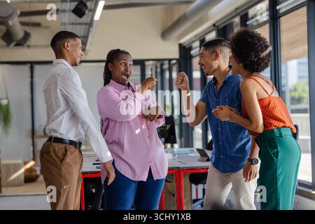 I colleghi in ufficio ridono e si impegnano in una conversazione vivace vicino alla finestra Foto Stock