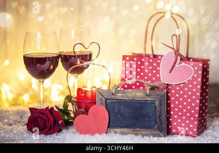 Borsa regalo, rosa rossa e bicchieri da vino rossi pieni su neve artificiale, composizione Foto Stock
