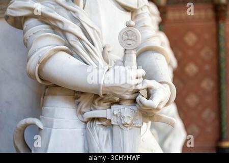 Primo piano su mani maschili con una spada di scultura in marmo che rappresenta un antico soldato crociato Foto Stock