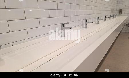 Moderno bagno pubblico con pareti piastrellate bianche e rubinetti cromati Foto Stock