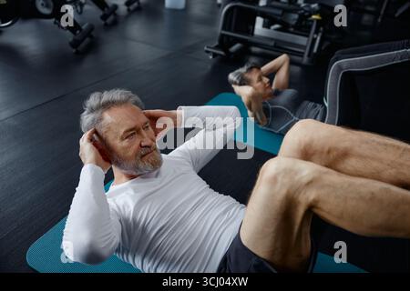 L'uomo si siede su un tappetino all'interno di una palestra Foto Stock